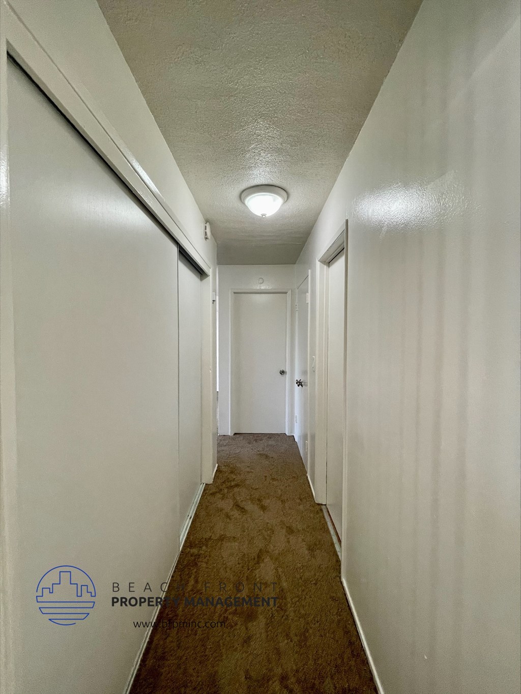 a long hallway with white walls and a wooden floor with a white door and a